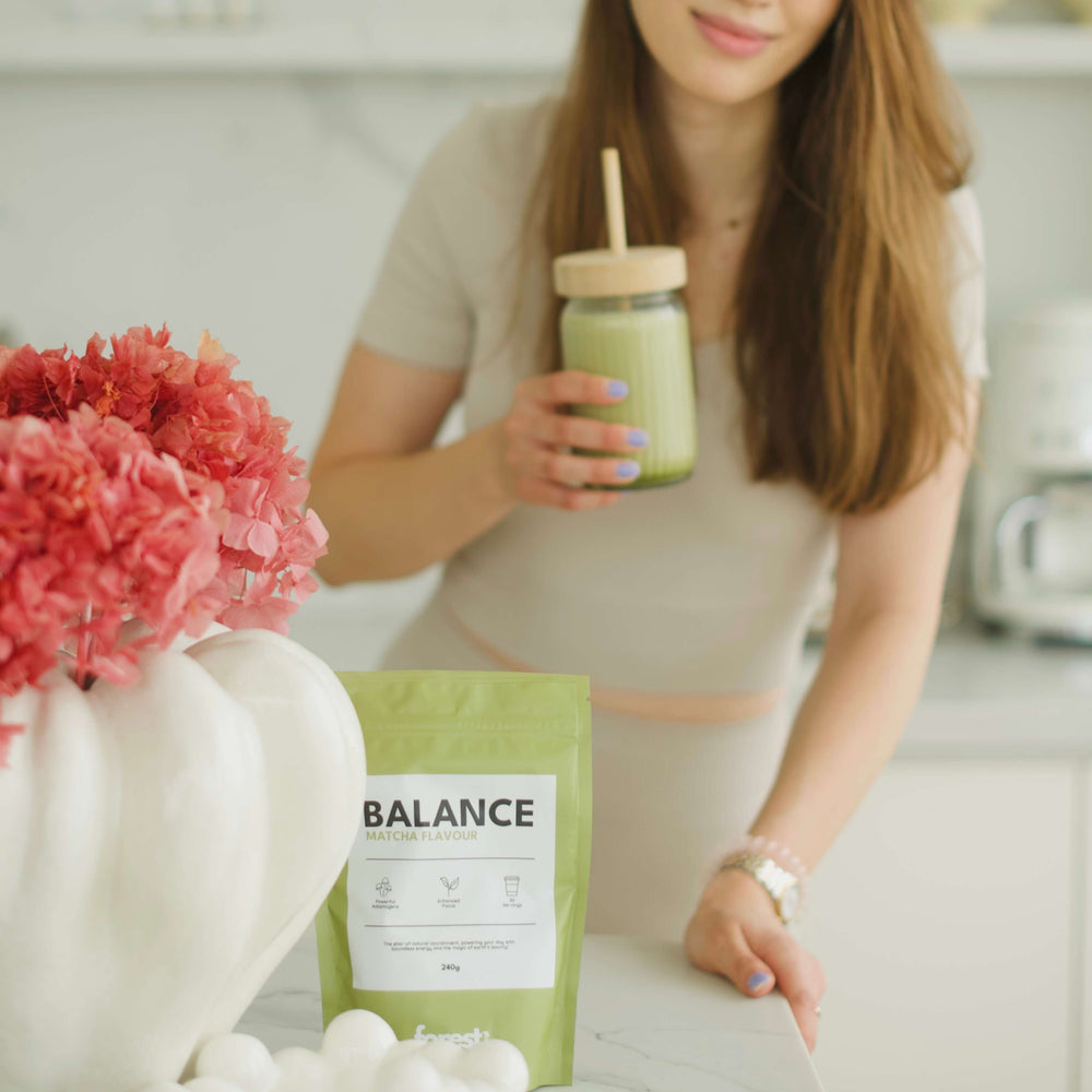 Woman holding a green smoothie with a 'Balance' package in a kitchen setting
